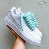 Custom all-white sneakers featuring thick mint green rope laces, displayed against a textured wall background

